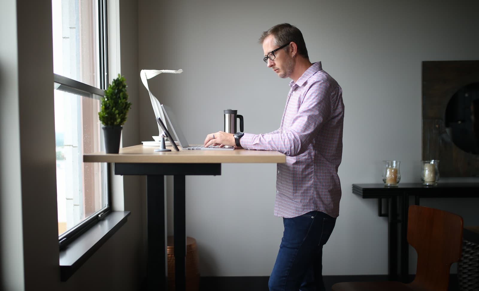 Standing Desks - man in pink dress shirt and blue denim jeans standing beside brown wooden table